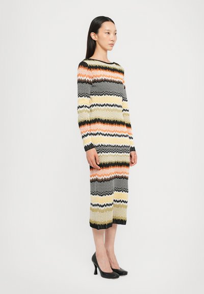 Abito a maglia con motivo a zigzag in arancione, verde, nero e bianco. Maniche lunghe, scollatura a girocollo, lunghezza fino al ginocchio e polsini a coste.