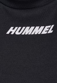Czarna koszulka z wysokim kołnierzem wykonana z gładkiej tkaniny, z wyraźnie widocznym białym logo "HUMMEL" na przodzie.