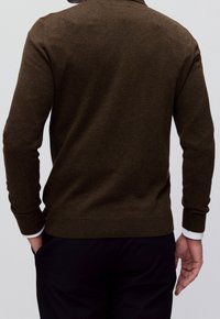 Pull-over marron en maille avec un col, des poignets et un ourlet côtelés. Coupe ajustée avec une texture lisse, associé à un pantalon noir.