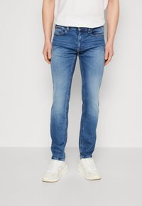 Blå denimjeans med smal passform, femficksdesign och lätt blekning. Kombinerade med vita sportiga sneakers, som visar en avslappnad stil.