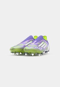 Scarpe da calcio viola e verdi con un design elegante, caratterizzate da una parte superiore texturizzata, stile slip-on anteriore e tacchetti trasparenti.