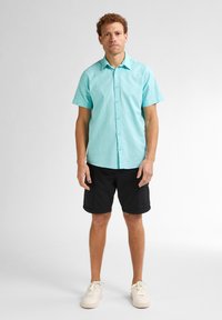 Turqoise kortemouw overhemd met een kraag, gecombineerd met zwarte shorts en witte sneakers. Het overhemd is gemaakt van een soepele, lichte stof.