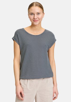 Top leggero a maniche corte in nero con motivo a pois bianchi; scollatura rotonda e vestibilità comoda. Abbinato a pantaloni beige chiaro.