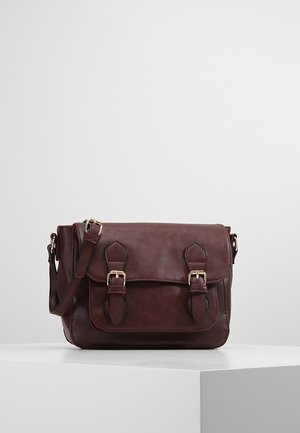 Braune Ledertasche mit verstellbarem Schulterriemen und zwei vorderen Schnallenverschlüssen, präsentiert auf einem weißen Sockel vor schlichtem Hintergrund.