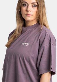 Paarse coton T-shirt met korte mouwen, een ronde halslijn en een klein wit "PEGADOR" logo op de borst. Soepele textuur.
