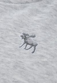 Mali sivi vezeni los sa rogovima na svijetlosivom teksturiranom pozadinskom materijalu.