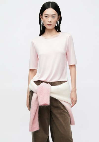 Light pink short-sleeve t-shirt paired with brown corduroy pants, featuring a soft, color-blocked knit scarf tied around the waist.