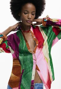 Meer-kleurig overhemd met levendige patronen in rood, groen, roze en oranje, met een losse pasvorm en een knoopsluiting.