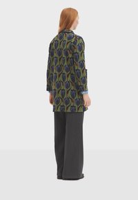 Longue veste avec un motif floral vert, bleu et violet. Portée sur une chemise bleue. Associe avec un pantalon large à rayures verticales sombres.