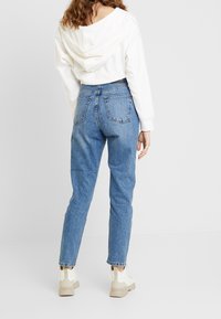 Ljusblå jeans med hög midja och rak ben, med femficksdesign och fransad nederkant. Kombineras med en vit huvtröja.