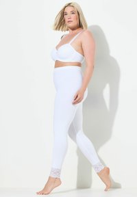 Soutien-gorge blanc rembourré et leggings blancs avec des détails en dentelle au niveau des chevilles. Les leggings ont une texture lisse et une taille élastique.