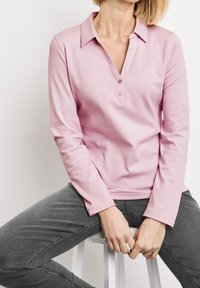 Rosa Langarm-Polohemd mit Kragen, ausgestattet mit einer Knopfleiste mit drei Knöpfen und einer glatten, weichen Textur. Getragen mit grauen, figurschmeichelnden Jeans.
