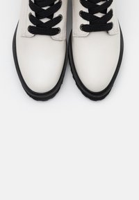 Sneaker bianchi in pelle con lacci neri e suole in gomma, caratterizzati da punte arrotondate e una texture liscia. Design semplice e minimal.