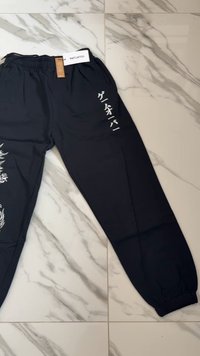 Zwarte joggers met witte grafische ontwerpen, voorzien van een elastische tailleband en boorden. Gemaakt van een gladde stof met een lichte glans.