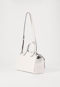 Sac à main en cuir blanc avec un design structuré, de courtes poignées doubles, une longue sangle amovible et des accents noirs autour de la fermeture éclair.