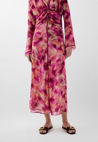 Long, flowing dress in a pink and orange abstract pattern; sheer fabric with long sleeves and a ruched bodice detail. Brown sandals with gold accents.