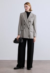 Διπλόστενο καρό σακάκι σε μπεζ και μαύρο, συνδυασμένο με μαύρο παντελόνι φαρδιάς γραμμής. Ολοκληρωμένο με μαύρη στρογγυλή τσάντα και μοκασίνια.