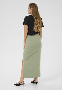 Longue jupe de couleur vert sauge en tissu doux, avec une fente latérale. Associée à un haut noir à manches courtes et des chaussures à talons kitten noires.