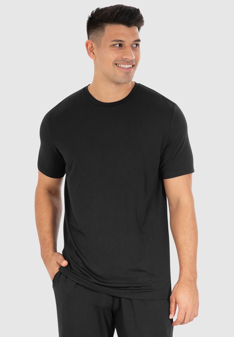 Sort kortærmet t-shirt i glat bomuld med rund halsudskæring og afslappet pasform, parret med sorte bukser, præsenteret mod en neutral baggrund.
