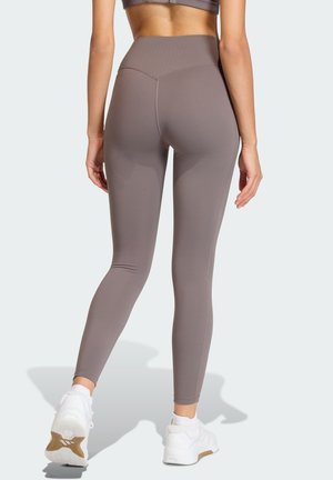 High-waisted, form-fitting leggings in taupe fabric, featuring a smooth texture and seams along the back. Paired with white athletic shoes.
