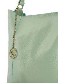 Lichtgroene leren tote bag met een gestructureerd oppervlak, voorzien van een goudkleurige ketting en een ronde accent tag, en contrasterende stiksels.