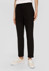 Pantalon noir slim en tissu léger. Présente un ourlet roulé et une fermeture à un bouton. Assorti à des baskets de couleur claire.