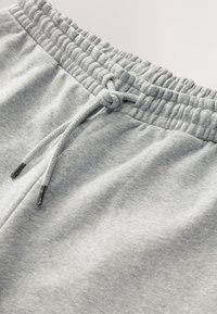 Pantalon de survêtement en coton gris avec une ceinture élastique et un cordon de serrage. Présente une texture douce et une surface lisse, avec des embouts métalliques sur le cordon.