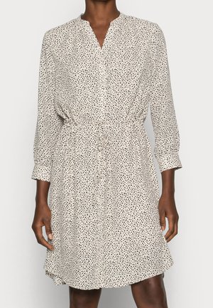 Korte mouwen, beige jurk met subtiel zwart polkadotpatroon, V-hals, elastische taille en een ontspannen pasvorm. Lichtgewicht stof met een vloeiende zoom.