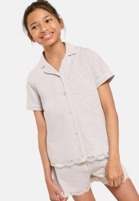 Ensemble de pyjama court gris clair en tissu doux. Comprend des passepoils blancs, une poche sur la chemise, et des finitions en dentelle sur le short et le haut.