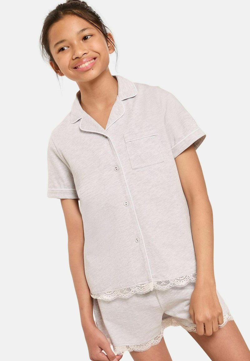 Ensemble de pyjama court gris clair en tissu doux. Comprend des passepoils blancs, une poche sur la chemise, et des finitions en dentelle sur le short et le haut.