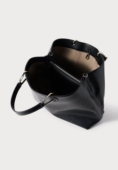 Μαύρη δερμάτινη τσάντα tote με απαλή υφή, ευρύχωρο εσωτερικό και διαμερίσμα με φερμουάρ. Διαθέτει ασημένια μεταλλικά στοιχεία και μια ενιαία λαβή.