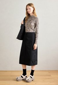 Pikend varrukatega topp beeži ja musta keerleva mustriga, koos musta utiliitse seeliku juures. Kantud paksude kreemjate platvormsandaalidega.