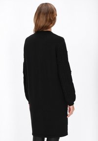 Lungo vestito maglione nero con maniche a trecce testurizzate e dettagli di perline. Corpo liscio e orlo a coste per un tocco in più.