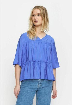 Blouse à col en V à manches courtes, de couleur bleu vif. Tissu texturé avec un design évasé et superposé. À associer avec un jean en denim clair.