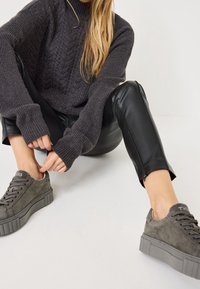 Pull en maille gris avec texture côtelée, pantalon en cuir noir, et baskets compensées en daim gris avec lacets et logo sur le côté.