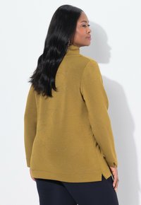 Suéter amarillo dorado con mangas largas, cuello alto y un sutil patrón floral. Presenta aberturas laterales y una tela texturizada con brillos.