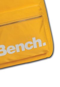 Sac en nylon jaune avec une texture lisse, présentant une poche avant à zip et un logo blanc audacieux portant la mention "Bench."
