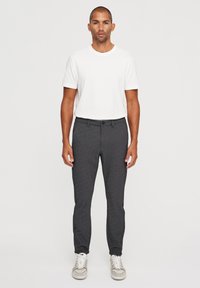 Pantalones grises ajustados con una textura suave, bolsillos frontales y un cierre de un solo botón, combinados con una camiseta blanca simple y zapatillas.