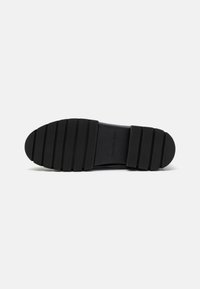 Semelle de chaussure en caoutchouc noir avec un motif strié, présentant un léger talon et le nom de marque embouti "Calvin Klein Jeans". Texture lisse.