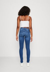 Tynne blå jeans med høy liv, laget av denim. Bak vises det to lommestifter og en brun lærmerke på livlinjen.