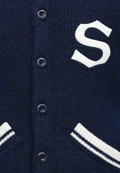 Navy neulejakku, jossa on valkoiset raidalliset resorit. Isot valkoiset brodeeratut "S"-logot. Varustettu tummilla muovinhopeilla ja kahdella etutaskulla.