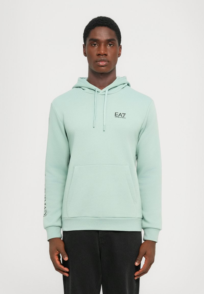 Mint green hoodie with front pocket, drawstrings, and black EA7 logo on chest. Long sleeves feature a printed design. Soft fabric texture.