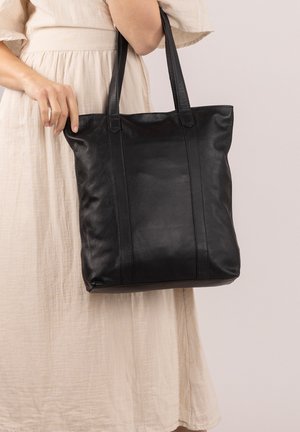 Zwarte leren tote bag met verticale naaddetails en twee stevige handvatten. Het materiaal is glad met een zachte textuur en minimale hardware.