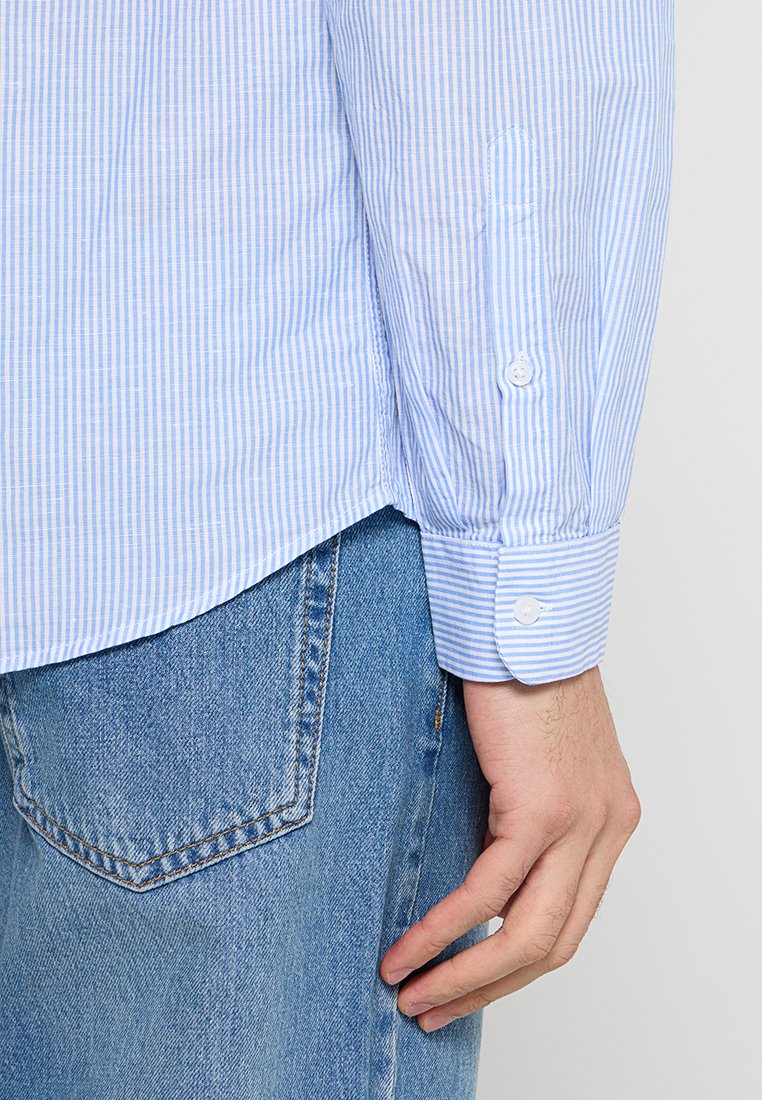 Camicia a righe blu chiaro e bianca con maniche risvoltate e due bottoni, abbinata a jeans di denim blu.