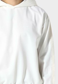 Felpa bianca con cappuccio dallo stato morbido, caratterizzata da un pannello laterale di colore neutro e un logo del marchio discreto sul petto.