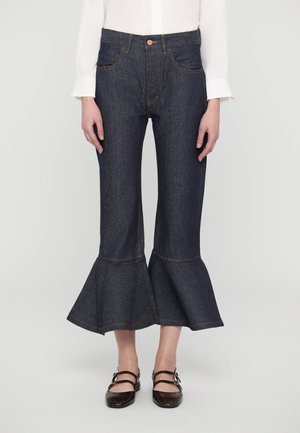 Dark blue denim flared jeans featuring a fitted waist, front pockets, and a ruffled bottom hem with orange stitching details.