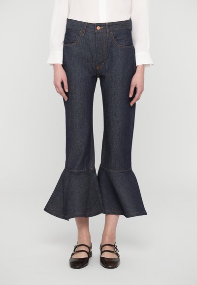 Vaqueros acampanados de denim azul oscuro con cintura ajustada, bolsillos frontales y un dobladillo con volantes en la parte inferior, adornado con detalles de costura naranja.