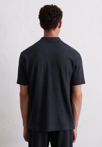 Dunkelblaues Poloshirt mit strukturierten vertikalen Streifen, kurzen Ärmeln und klassischem Kragen. Schlichte Rückansicht, der Stoff wirkt gestrickt.