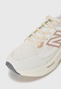 Letvægt løbesko med en mesh-overdel i off-white og bløde lyserøde accenter, der har en polstret sål og synlig branding på siden.