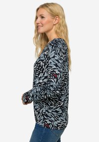 Langarmshirt in marineblauw met een patroon van lichtblauwe bladeren. De stof lijkt zacht, heeft een relaxed fit en subtiele rode accenten.